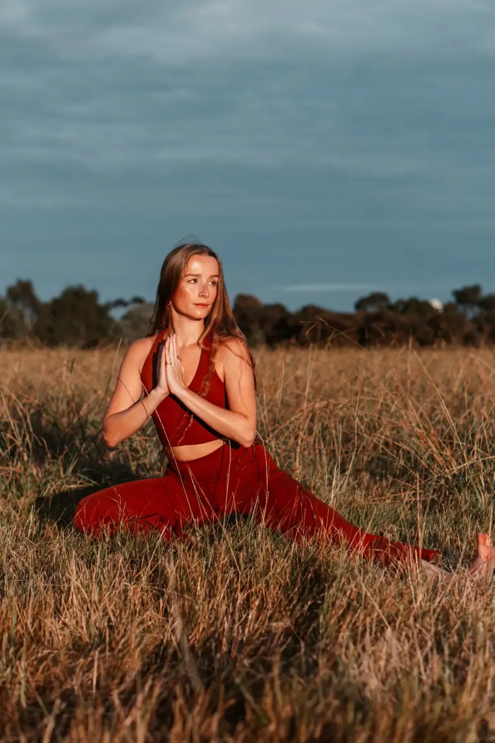 Indra-Kaye Staunton seated in a twist with hands in prayer position, in a grassy field